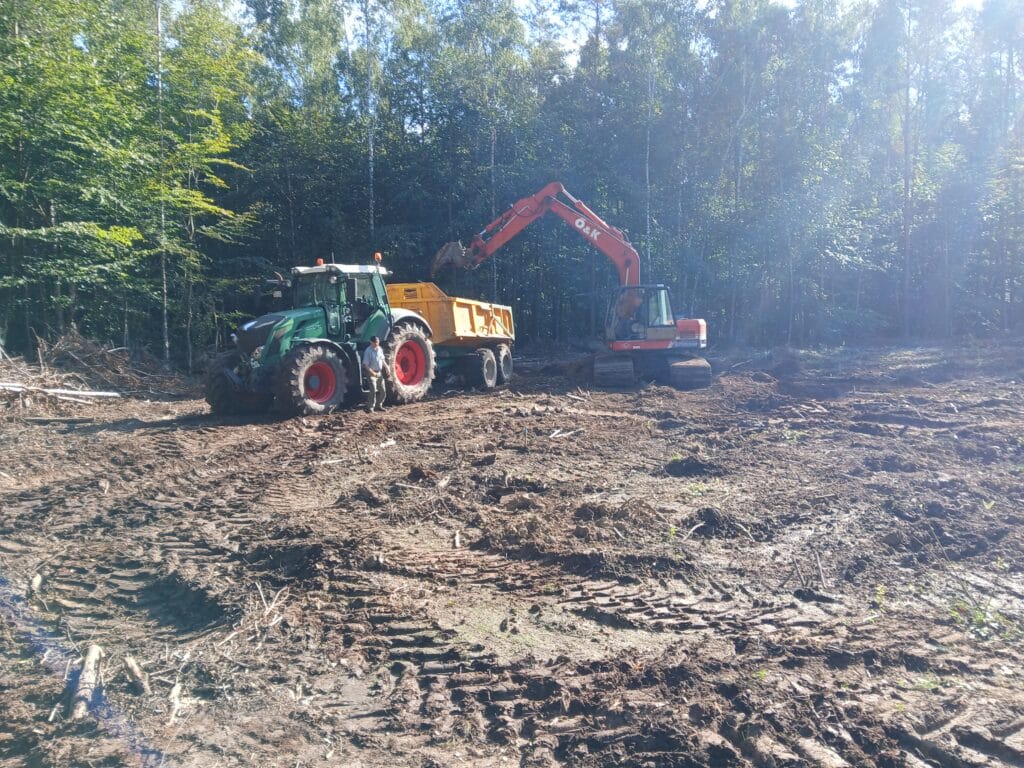 Ein Bagger belädt einen Trecker mit Muldenkipper mit dem Aushub des anzulegenden Teiches im Wald.